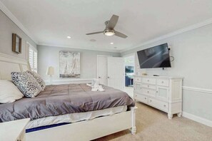 Une chambre à coucher avec un lit, un ventilateur de plafond, une télévision, une commode et un tableau accroché au mur.