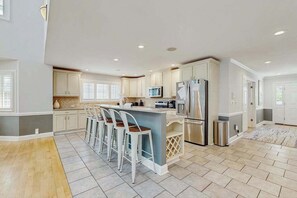 A spacious kitchen with a central island, bar stools, and modern appliances. - Salt Pond house with W/D, pools, & hot tub - near beach & dining (Bethany Beach)