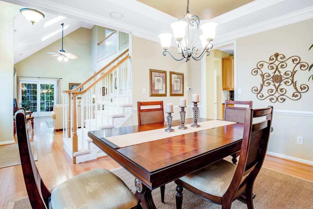 A dining area with a wooden table, chairs, a chandelier, and a staircase leading to another level.