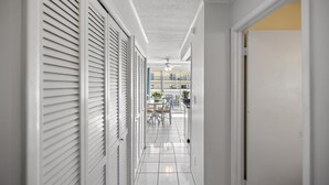Um corredor com paredes brancas, chão ladrilhado e uma porta que dá para uma varanda com mobiliário de exterior.