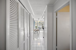 Ein Flur mit weißen Wänden, gefliestem Boden und einer Tür zu einem Balkon mit Gartenmöbeln.