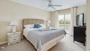 A bedroom with a bed, ceiling fan, bedside lamps, a TV, and a balcony with curtains. - Three-Story Bayside Resort Retreat W/ Shared Pool/Hot Tub, Balcony & Central AC (Selbyville)