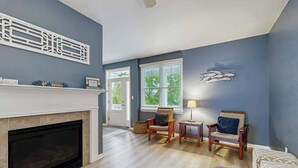 A living room with a fireplace, two armchairs, a side table, and a wall-mounted artwork. - Three-Story Bayside Resort Retreat W/ Shared Pool/Hot Tub, Balcony & Central AC (Selbyville)