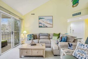 A living room with a sofa, a coffee table, a painting of a beach, and a sign that says 'BEACH HOUSE'. - Sea Colony Condo w/ Free WiFi, Central AC, Shared Pools, & Hot Tubs (Bethany Beach)