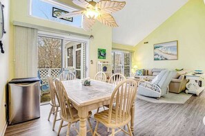 A dining area with a wooden table and chairs, a ceiling fan, and a view through large windows. - Sea Colony Condo w/ Free WiFi, Central AC, Shared Pools, & Hot Tubs (Bethany Beach)