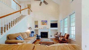 A spacious living room with a staircase, a fireplace, and a television. - Bear Trap Dunes Townhouse Near Bethany Beach w/Shared Pool, Free WiFi, W/D (Ocean View)