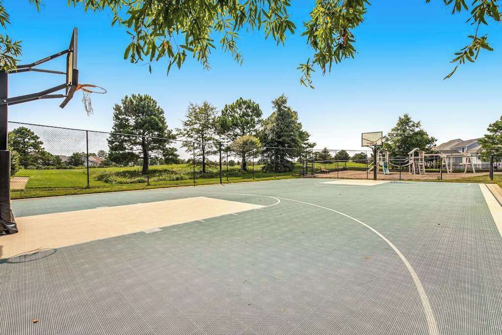 Un terrain de basket en plein air, équipé d’un panier, entouré d’arbres et d’une clôture.