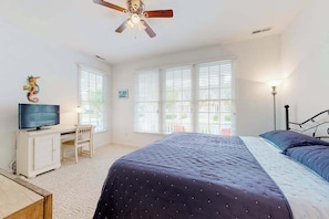 A bedroom with a bed, a desk, a chair, a television, and a ceiling fan.