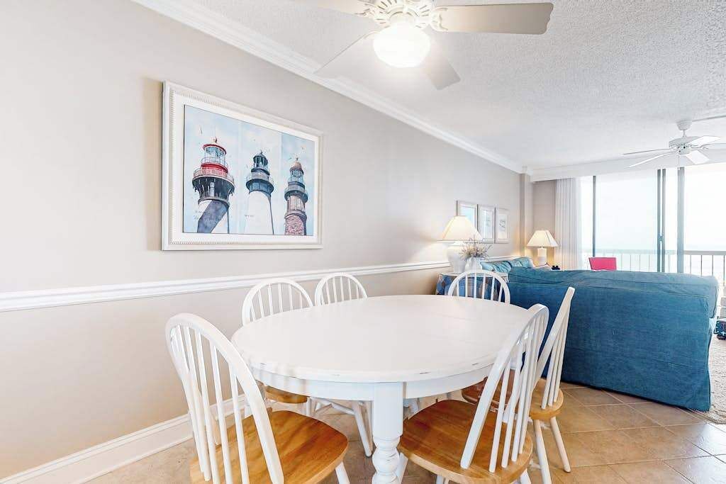 A dining area with a white table and chairs, a ceiling fan, and a large window with a view.
