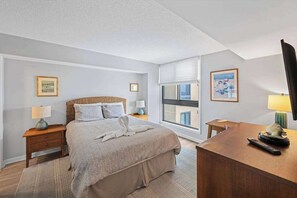 A bedroom with a bed, bedside tables, a desk, a window, and artwork on the walls. - Sea Colony Ocean condo with shared pools, hot tubs, beach access & balcony (Bethany Beach)