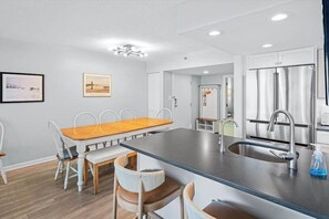 A modern kitchen with a central island, stainless steel appliances, and a dining area with white chairs. - Sea Colony Ocean condo with shared pools, hot tubs, beach access & balcony (Bethany Beach)