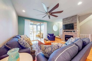 Ein Wohnzimmer mit Deckenventilator, Kamin, Fernseher und Sofagarnitur.