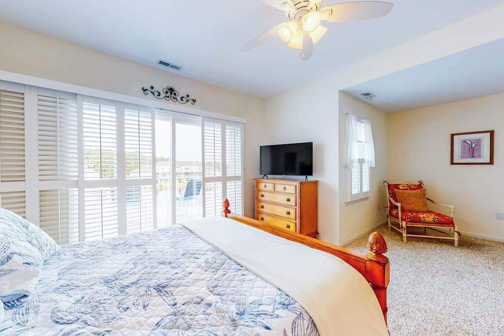 Um quarto com cama, cômoda, televisão, cadeira e ventilador de teto.