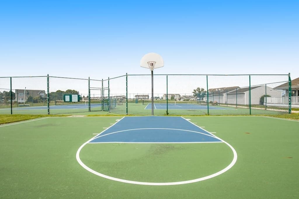 An outdoor basketball court with a hoop, surrounded by a fence.