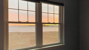Een kamer met een groot raam met uitzicht op een strand en een verre skyline.
