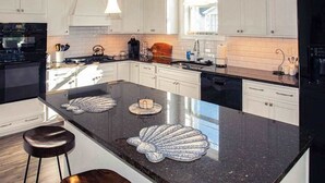 Ett modernt kök med vita skåp, en svart bänkskiva i granit och en stor köksö dekorerad med vackra snäckskal.