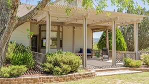 Une terrasse couverte avec une pergola, des sièges d’extérieur et une vue sur une maison.