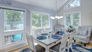 A dining area with a table set for four, white chairs, a chandelier, and large windows. - Dog-friendly home close to the beach w/balcony, fireplace, grill, AC (Bethany Beach)