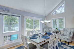 A dining area with a table set for four, white chairs, a chandelier, and large windows. - Dog-friendly home close to the beach w/balcony, fireplace, grill, AC (Bethany Beach)
