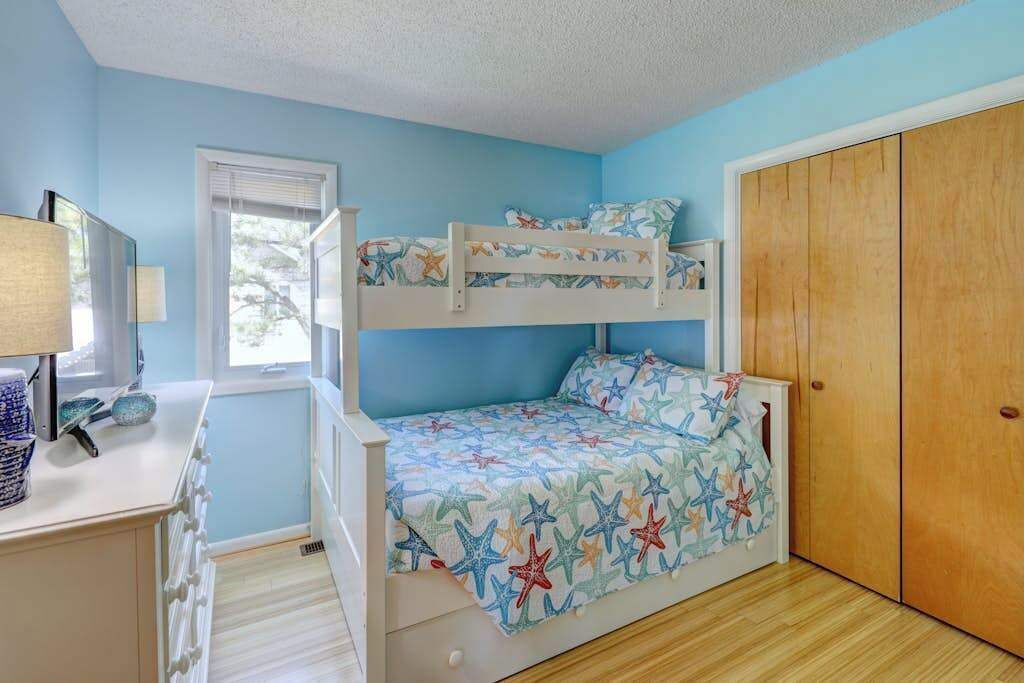 Una camera con un letto a castello, una coperta a motivi stellari, un armadio in legno e una scrivania con una lampada.