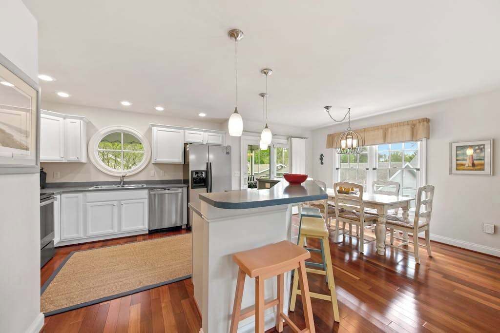 A modern kitchen with white cabinets, a central island, pendant lighting, and a dining area with a table and chairs.