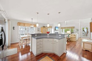 A modern kitchen with a central island, wooden dining table, and pendant lighting. - Bethany West home with grill, washer/dryer, WiFi, central AC, & pool (Bethany Beach)