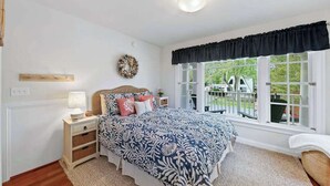 Un dormitorio con una cama grande, una mesita de noche, una lámpara, una ventana con vistas y una corona decorativa en la pared.