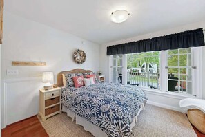 A bedroom with a large bed, a nightstand, a lamp, a window with a view, and a wall-mounted wreath. - Bethany West home with grill, washer/dryer, WiFi, central AC, & pool (Bethany Beach)