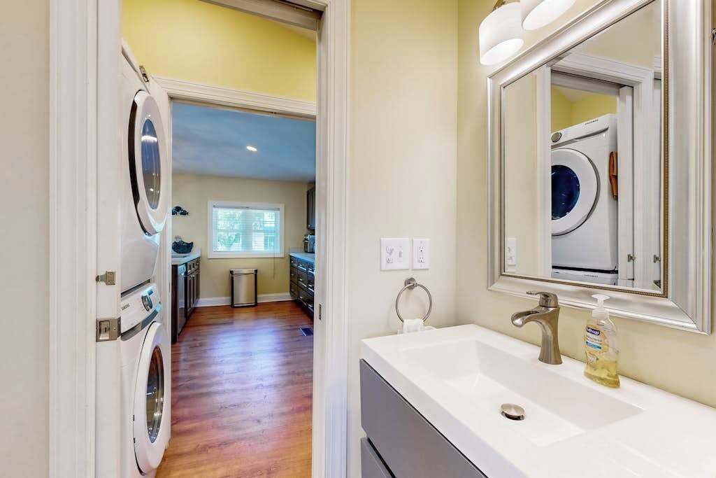 A laundry room with a washing machine and dryer, a sink with a mirror, and a window with blinds.
