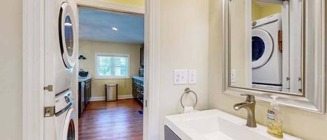 A laundry room with a washing machine and dryer, a sink with a mirror, and a window with blinds.