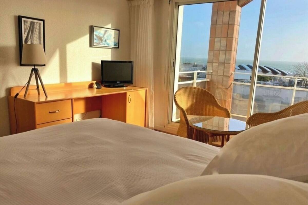 Hotelkamer met een bed, een bureau met een computer, een stoel en uitzicht over de stad.