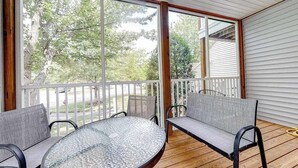 A covered outdoor area with a round glass table and two cushioned chairs, a wooden deck, and a white railing. - Sea Colony Tennis condo w/ central AC and access to pool and fitness center (Bethany Beach)