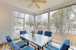 A covered patio with a table and chairs, large windows, and a ceiling fan.
