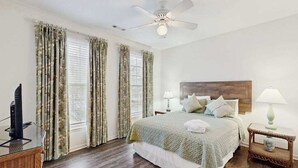 A hotel room with a bed, two bedside tables with lamps, a ceiling fan, and a television on a stand. - Coastal Retreat I Resort Amenities, Championship Golf, Indoor & Outdoor Pools (Ocean View)