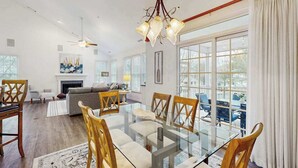 A spacious living room with a glass dining table, wooden chairs, a fireplace, and large windows. - Coastal Retreat I Resort Amenities, Championship Golf, Indoor & Outdoor Pools (Ocean View)