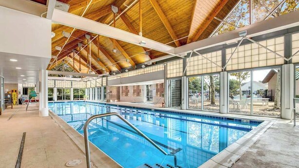 An indoor swimming pool with a wooden ceiling, clear glass walls, and a concrete floor. - Coastal Retreat I Resort Amenities, Championship Golf, Indoor & Outdoor Pools (Ocean View)