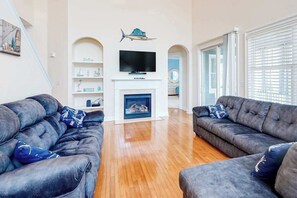 A living room with two dark sofas, a fireplace, a flat-screen TV, and a decorative fish on the wall. - Bayside Resort home close to the beach with shared pools & hot tub - dogs OK (Selbyville)