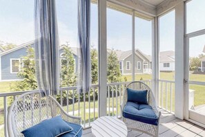 A covered porch with wicker chairs and a small table, overlooking a residential neighborhood. - Bayside Resort home close to the beach with shared pools & hot tub - dogs OK (Selbyville)