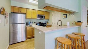 Una cocina moderna con armarios de madera, electrodomésticos de acero inoxidable, una isla central con taburetes y una puerta blanca.
