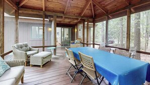 Un espacio al aire libre techado con una mesa, sillas, vigas de madera y ventanas grandes.