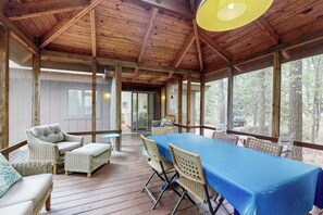 Un espacio al aire libre techado con una mesa, sillas, vigas de madera y ventanas grandes.