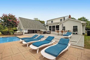 Ein Garten mit Swimmingpool, Liegestühlen, Grillplatz und einer überdachten Terrasse.