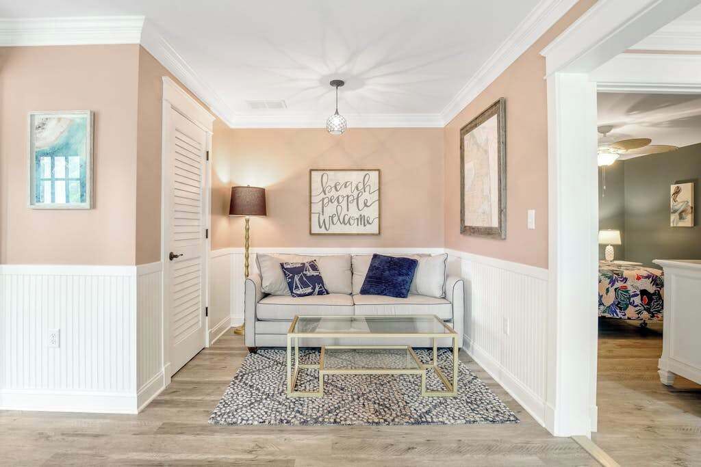 Un salon comprenant un canapé, une table basse, un tapis, une œuvre d’art murale et une porte.