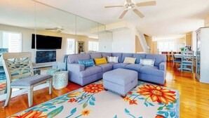 Ein Wohnzimmer mit Ecksofa, Fernseher, Deckenventilator und Essbereich mit Tisch und Stühlen.