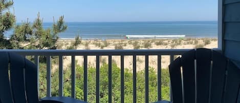 A balcony with a view of the beach, chairs, and a railing.