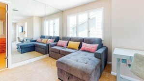Ein modernes Wohnzimmer mit einem Ecksofa, einem kleinen Tisch und einem Spiegel, der den Raum widerspiegelt.
