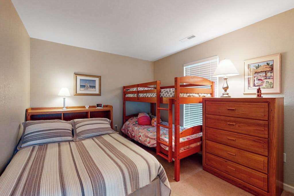 A bedroom with a bunk bed, a bedside table with a lamp, a dresser, and a framed picture on the wall.