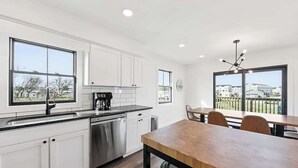 Une cuisine moderne avec des meubles blancs, un lave-vaisselle en acier inoxydable et une table à manger en bois avec des chaises.