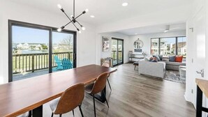Un vaste espace de vie comprenant une table à manger en bois, un canapé gris et une vue sur l’extérieur.