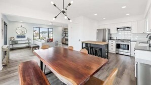 Une cuisine moderne avec des meubles blancs, des appareils en acier inoxydable et une table à manger en bois.